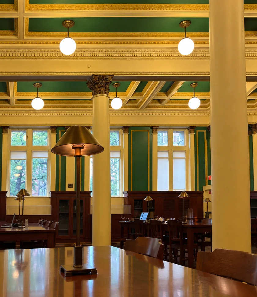 Wooden tables and brass lamps beneath a green and gold ceiling in the library’s quiet reading room.